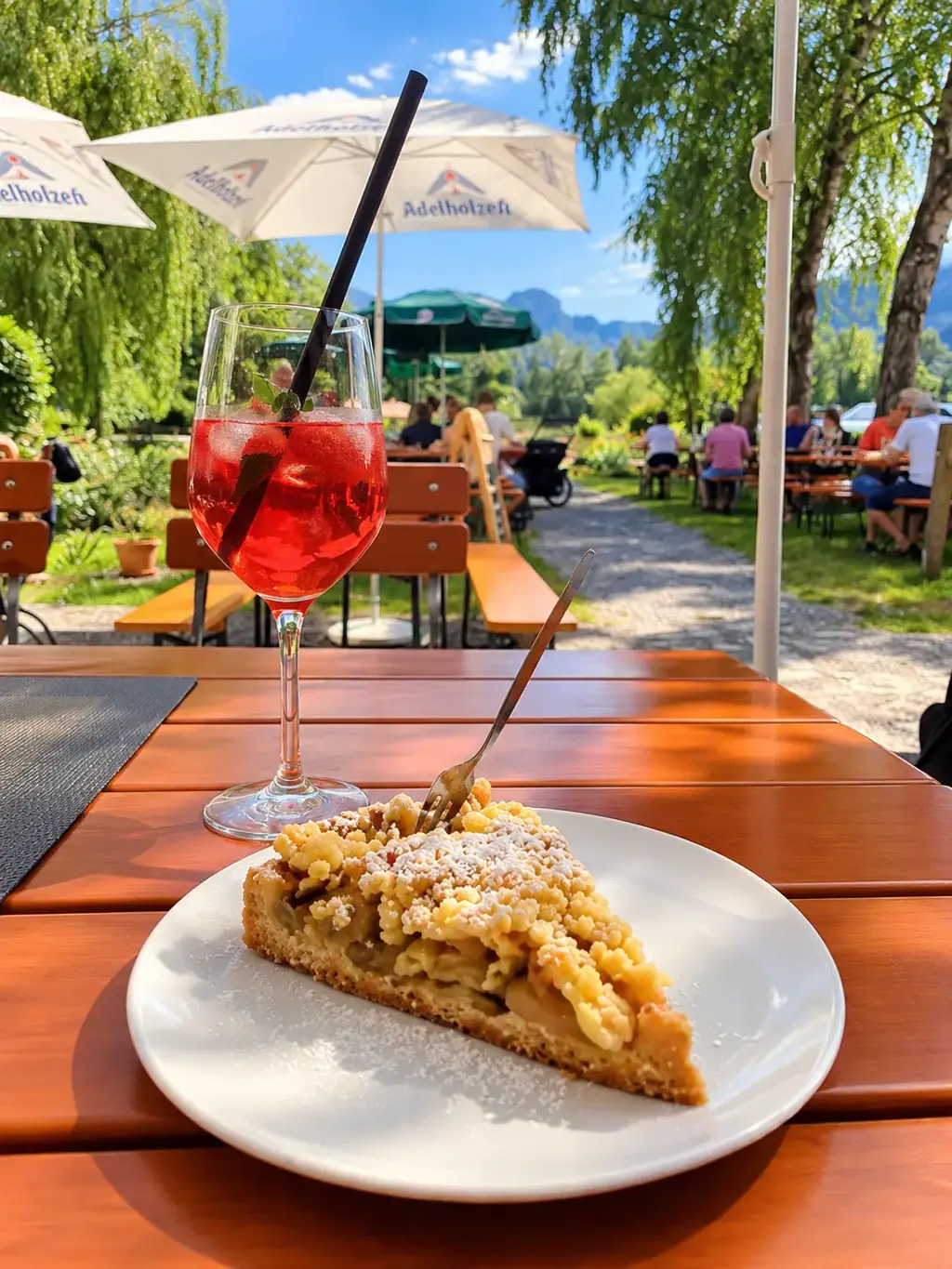 Stück Apfelstreuselkuchen und ein Spritz auf einem Holztisch im Biergarten