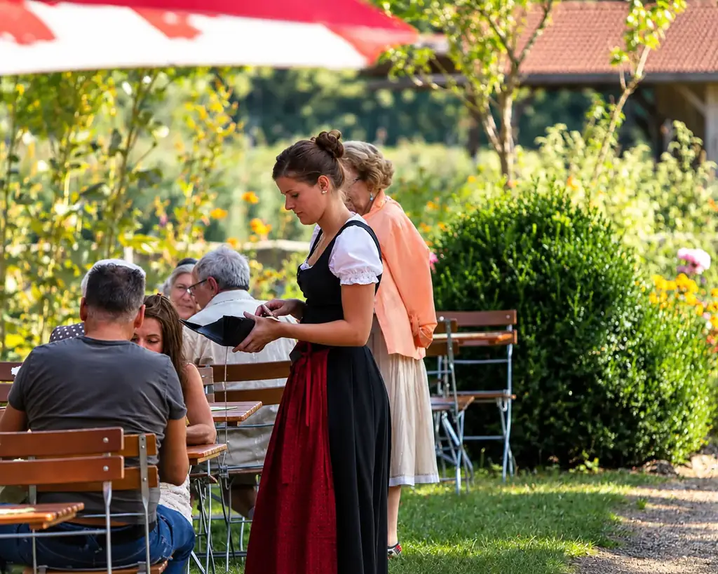 Bedienung im Dirndl kassiert an einem Tisch im sommerlichen Naturgarten
