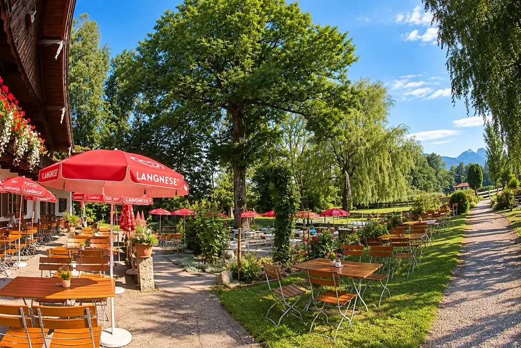Biergarten und Naturgarten der Moosmühle unter großen Laubbäumen, im Hintergrund die Berge