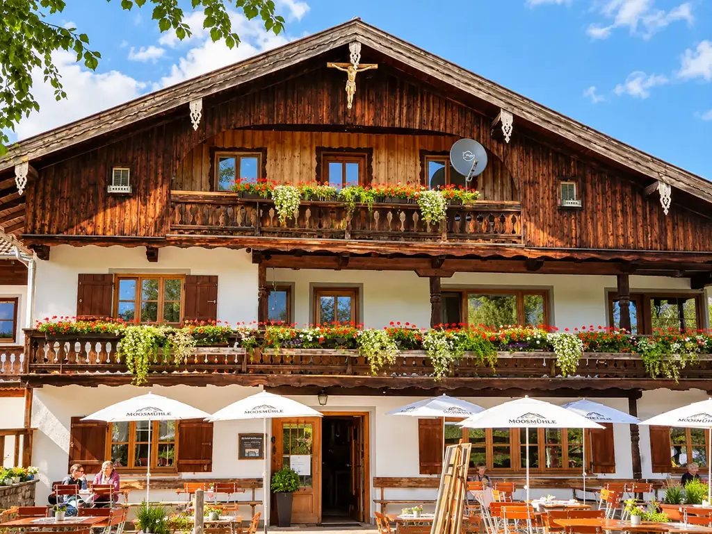 Holzfassade der Moosmühle mit Geranien an den Balkonen und Sonnenschirmen vor dem Eingang