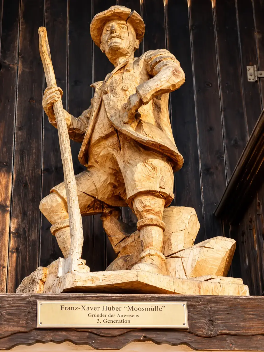 Geschnitzte Holzfigur von Franz-Xaver Huber „Moosmülle“ an der Hauswand