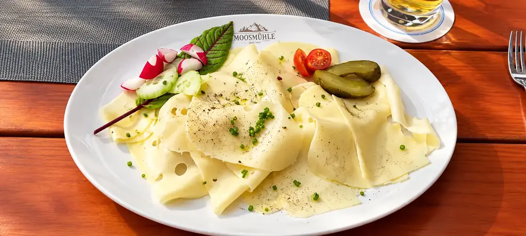 Käseteller mit Schnittlauch, Radieschen und Gurken auf einem Holztisch im Freien